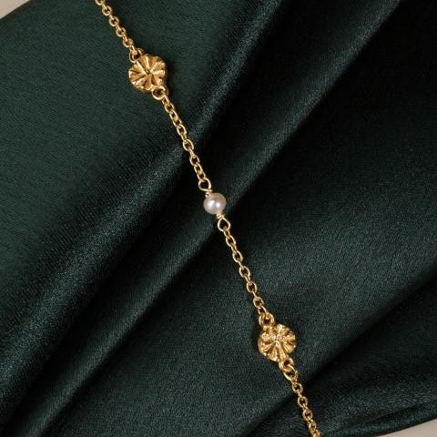 delicate chain with pearl and 2 flower beads in gold on dark green fabric