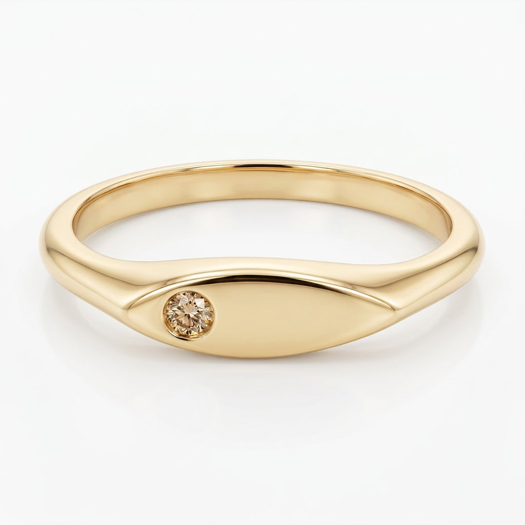 A yellow gold signet ring with a small round dark gemstone set on the front, photographed on a plain light gray background.
