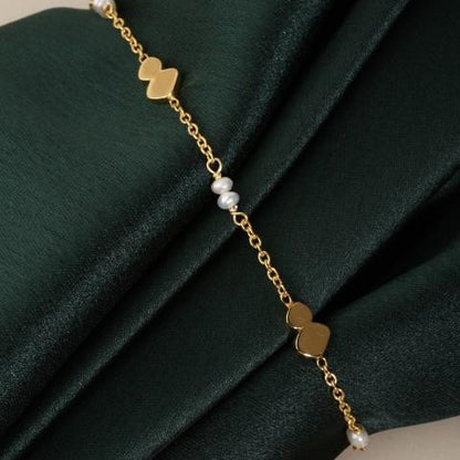 fine chain bracelet with small round white pearls and flat pebble sections around darg green fabric.
