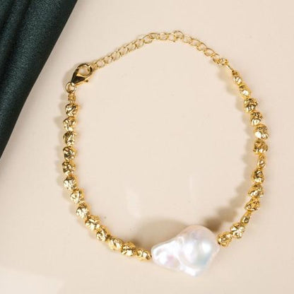 gold plated bracelet laying flat on a white background. The bracelet has a large gnarly looking pearl in the centre of rugged pebbly shaped beads. The bracelet has an extension chain and a cartier clasp.
