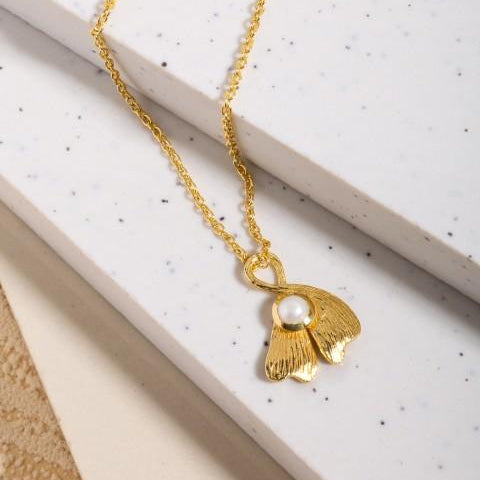 gold ginko leaf pendant on chain laying on white marble steps