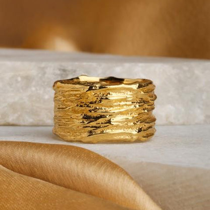Wide gold plated ring, ripple texture, sitting on white stone with gold satin ribbon curled in front